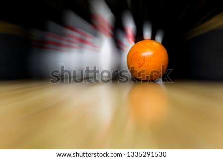 An orange bowling ball is rolling at great speed into white skittles. Copy space wooden bowling alley