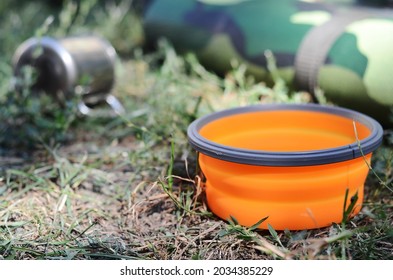 Orange camping folding silicone plate on the grass, mug and rug with blurred background.