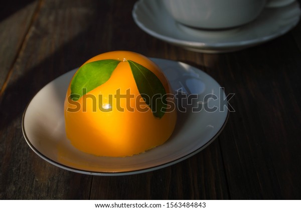 The orange car cake is on a white plate placed on\
a black wooden table.