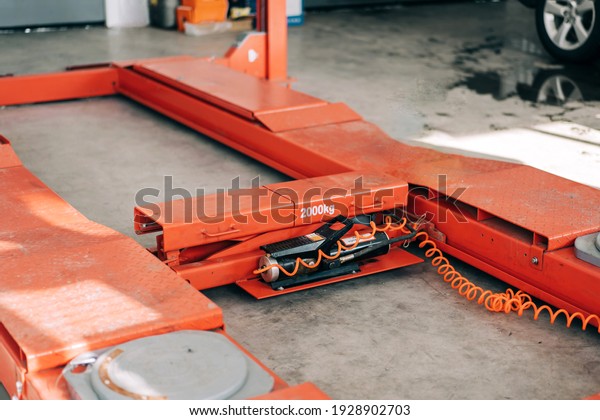 Orange car lift in a calm\
state for indoor use. Equipment at the service station for lifting\
machines.