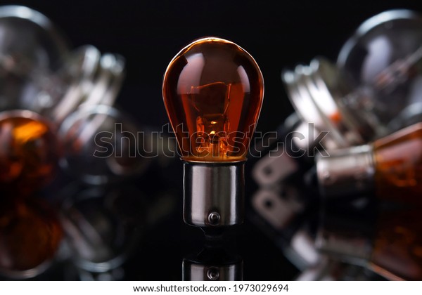 Orange car light bulb\
against blurred lamps on dark background, small depth of focus.\
Automotive parts.
