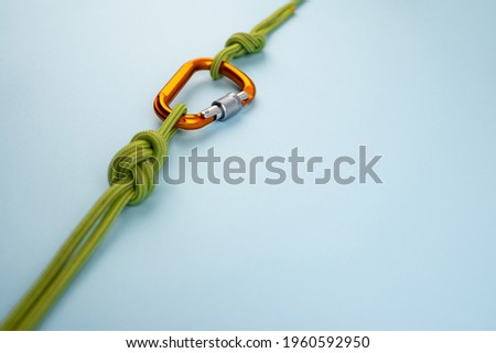 Orange Carabiner with rope. Equipment for climbing and mountaineering, alpinism, rappelling. Safety rope. Knot eight. Isolated on the blue background. Minimal concept, copy space.

