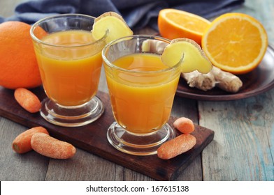 Orange and carrot juice in glass with ginger,  fresh vegetables and fruits on wooden background