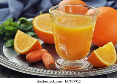 Orange and carrot juice in glass with mint,  fresh vegetables and fruits on round tray