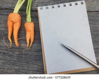 Orange Carrot Like Woman Shape Put Beside White Paper Note And Pen