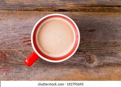 Orange Ceramic Mug Full Of Fresh Hot Latte Morning Coffee Topped With A Milky Froth , Overhead View On A Wooden Table With Copyspace