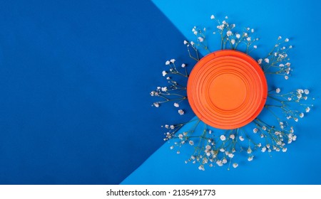 Orange Clay Target On White Gypsophila Flowers On Blue Geometric Background. Skeet Shooting. Mockup With Copy Space