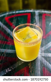 An Orange Cocktail In A Rocks Glass With A Big Ice Cube And Spicy Rim On The Glass