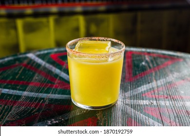 An Orange Cocktail In A Rocks Glass With A Big Ice Cube And Spicy Rim On The Glass