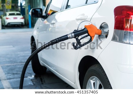 The orange color fuel nozzle filling oil into the white car