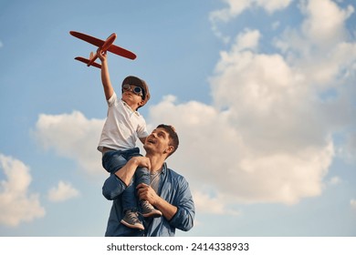 Orange colored toy plane in hands. Father and little son are playing and having fun outdoors. - Powered by Shutterstock