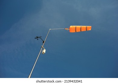 Orange conical windsock and wind cone - meteorologic device and tool on pole and post. Measuring and indicating wind during windy weather. Blue sky.