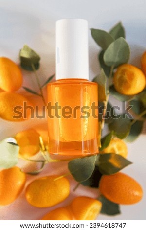 Orange cosmetic glass bottle with water drops, kumquat fruits and green eucalyptus leaves on a white background, mockup with copy space