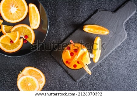 Orange cranberry fizzy cocktail in a glass and fruits next to it on a dark background. Homemade mocktail. Top view
