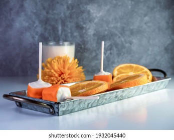 Orange creamsicle cake pops on a stick, orange and white dessert, delicious sweet treat with a glass of cold white milk and orange artificial flowers and fresh citrus orange fruit slices.