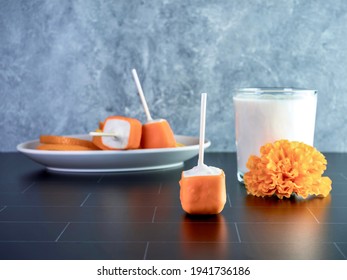 Orange creamsicle cake pops on a stick, orange and white dessert, delicious sweet treat with a glass of cold white milk and orange artificial flowers.