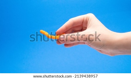 Orange Crunchy Cheese Puff Side View In Hand On A Blue Background