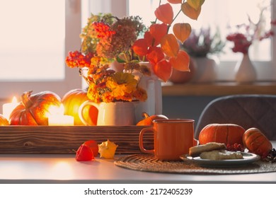 orange cup of tea and autumn decor with pumpkins, flowers and burning candles on table
