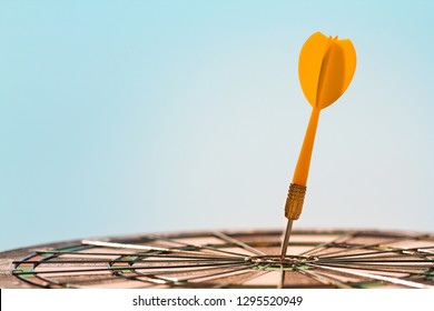 Orange dart arrow hitting bullseye in center target of dartboard on blue sky background with copy space. Business, strategy, achievement, and planning concept