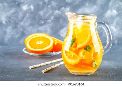 Orange detox water in a pitcher on a gray concrete background. Healthy food, drinks
