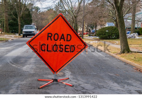 Orange diamond shaped road closure sign on road in\
a neighborhood near a\
house.