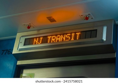An orange digital train display reads "NJ Transit" on one of the system's trains surrounded by a blue hue