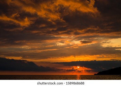 Orange dramatic cumulus clouds at sunset. Disk of the sun. Backlight