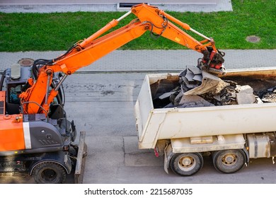 An Orange Excavator With A Bucket Loads The Old Pieces Of Asphalt Into A White Dump Truck