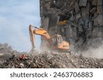 An orange excavator demolishes a building amidst rubble and debris, creating a dusty atmosphere at a construction site.