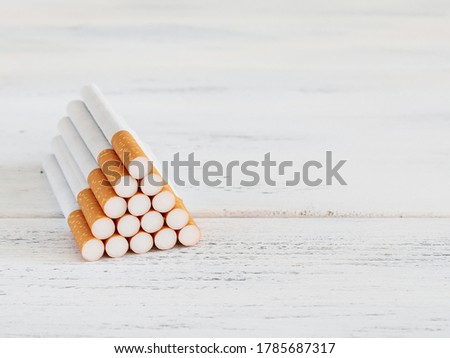 Orange filter cigarettes are lined up in a triangle on the left on a shabby white wooden table with space for text on the right, close-up side view.