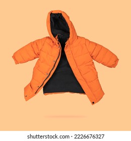 Orange flying children's winter autumn jacket with hood isolated on light orange background. Waterproof jacket for child, warm down jacket. Cutout clothing mockup. Fashion, style, outerwear - Powered by Shutterstock