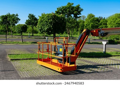 Orange forklift basket standing in an empty parking lot. Trees with green foliage in the background.
