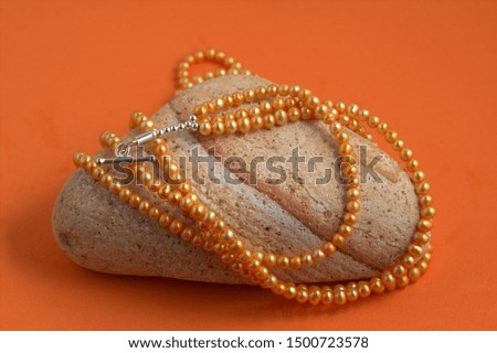 Orange freshwater pearl necklace on a stone and orange background