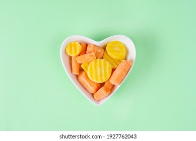 Orange Frozen Baby Carrot Mix In A White Heart-shaped Bowl On Light Green Background. Concept Love Vegetables, Vegetarian Food. Diet Ingredient, Top View. Healthy Meal Prep For Freezer Blank