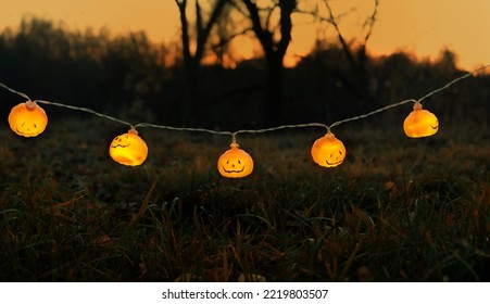 Orange glowing jack-o' lanterns garland on dark mysterious natural abstract background. symbol of Halloween holiday, Samhain sabbat. autumn season. - Shutterstock ID 2219803507