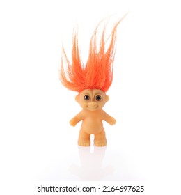 Orange haired troll doll or elf toy on a white background with reflection