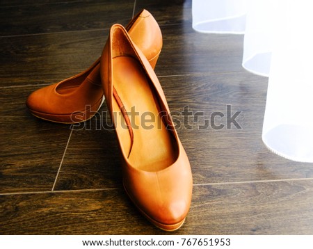 Orange high heels in different angle on brown laminate floor near white curtains