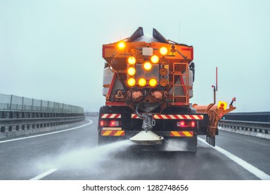 Orange Highway Maintenance Gritter Truck Spreading De-icing Salt On Road In Winter.