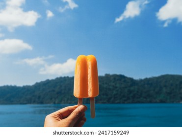 Orange ice creams on blue sky background. Orange popsicle in woman hand. Female hand holding melting Orange popsicle on a blue sky background in summer. - Powered by Shutterstock