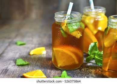 Orange iced tea in a glass jar with paper straws on a rustic wooden background.