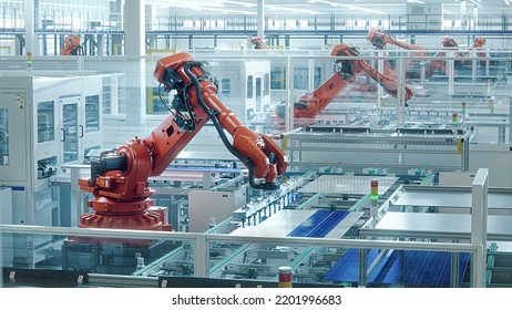 Orange Industrial Robot Arm At Production Line At Modern Bright Factory. Solar Panels Are Being Assembled On Conveyor. Automated Manufacturing Facility