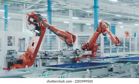 Orange Industrial Robot Arm At Production Line At Modern Bright Factory. Solar Panels Are Being Assembled On Conveyor. Automated Manufacturing Facility