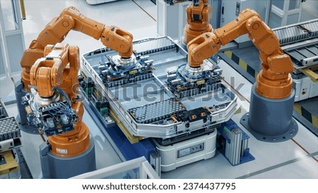 Orange Industrial Robot Arms Assemble Skateboard style EV Battery Pack on Automated Production Line. Electric Car Smart Factory Equipped with Robotic Arms. Battery Module Installation Process Top View