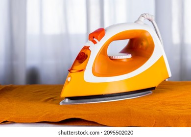 Orange iron and orange top on ironing board top view close up image.