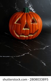 Orange jack o lantern displayed alone on a luxurious black marble background creating a sophisticated Halloween still life. The minimalist composition provides ample copy space for seasonal campaigns, branding and commercial design projects.