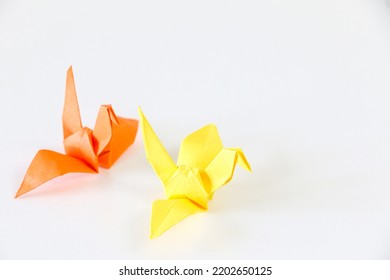 Orange Japanese Origami Paper Crane Follows Yellow One, On White Background