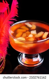 Orange Jello On A Beautiful Bowl With Fruit Pieces Inside. Black Background, Decorated With Pink Feathers.