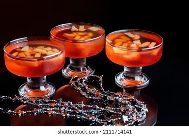 Orange Jello On A Beautiful Bowl With Fruit Pieces Inside. Black Background, Three Vases With Jelly.