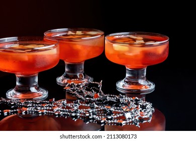 Orange Jello On A Beautiful Bowl With Fruit Pieces Inside. Black Background, Three Vases With Jelly. Side View.