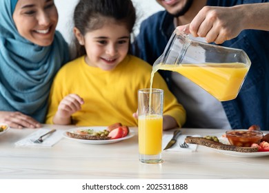 Orange Juice. Caring Man Pouring Healthy Vitamin Drink For His Daughter And Islamic Wife While They Having Lunch In Kitchen Together, Happy Middle Eastern Family Enjoying Tasty Meal Together At Home